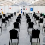 A large tent serves as a waiting area with rows of Conference Chair Black seats facing a clock, brightly illuminated by overhead lighting.