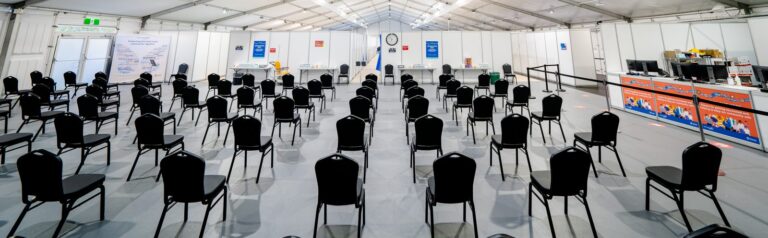 A large tent serves as a waiting area with rows of Conference Chair Black seats facing a clock, brightly illuminated by overhead lighting.
