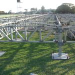 The Temporary Deck Sub Frame System is set up in a grassy field, likely for a platform or stage. Trees and a tower are visible in the background.