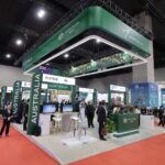 Wide view of an international expo hall featuring a large Australia booth with green overhead signage and many attendees exploring displays at counters and kiosks.