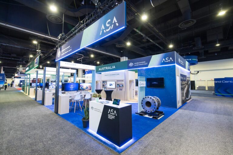 Trade show booth for the Australian Government's Australian Submarine Agency (ASA) with blue signage and displays on a blue carpeted floor.