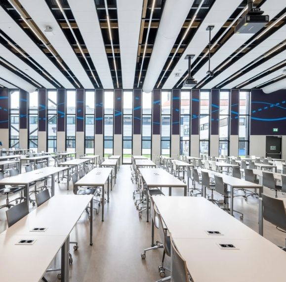 Bright modern study hall with rows of white tables and chairs, large windows along back wall.