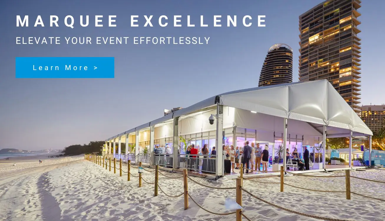 Beachside event marquee at dusk with guests inside; city skyscrapers in the background and a blue Learn More button.
