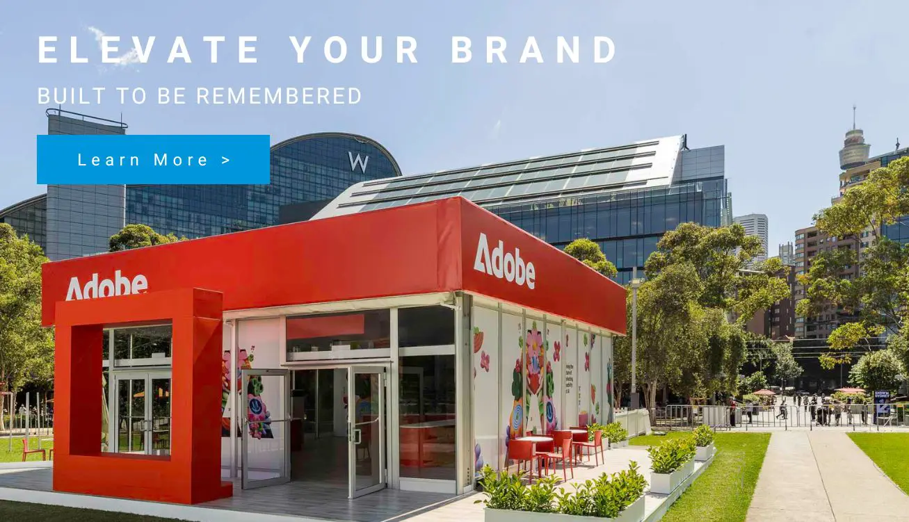 Adobe booth in a sunny city park: bright red storefront with colorful wall art and outdoor seating.