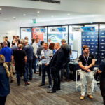 A busy tech expo hall with attendees networking around vendor booths and banners.