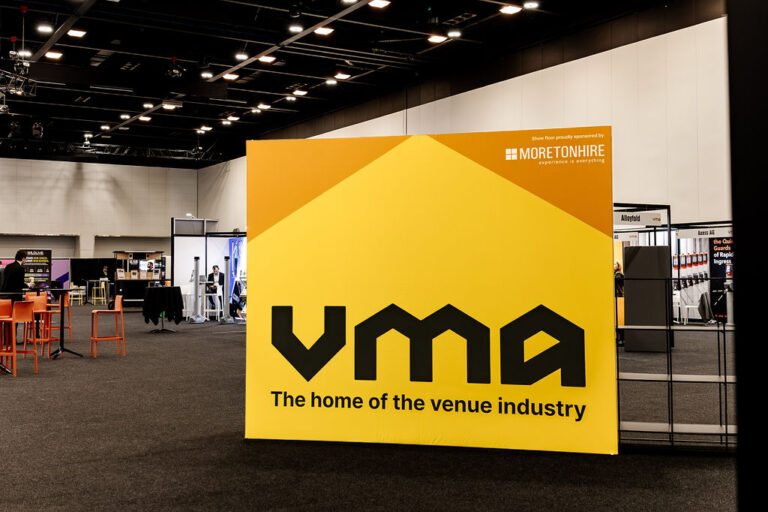 Large yellow VMF display panel at a convention hall featuring the slogan 'The home of the venue industry' and Moretonhire as sponsor.