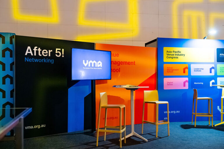 Trade show booth featuring After 5! Networking on a black panel, a VMA screen, and tall tables with stools.