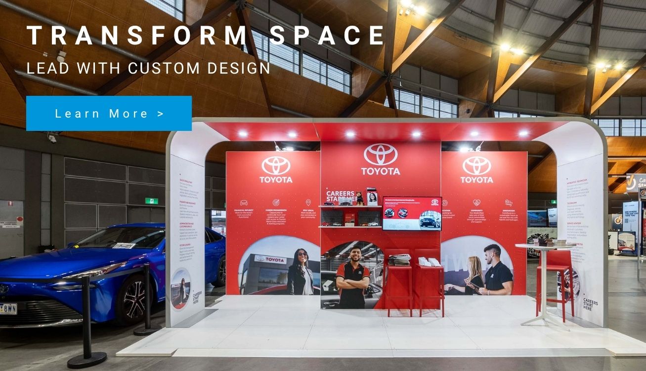 Promotional expo booth for Toyota with red display panels, a white curved frame, a blue car on the left, and a blue 'Learn More' button.