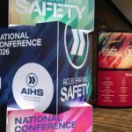 Colorful stacked conference signs reading 'National Conference 2026' with the AIHS logo visible, emphasizing safety topics in a hallway display.