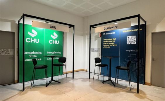 Two exhibition booths in a hallway: left booth shows CHU with green banners and stools, right booth shows Guidewire with blue banners and stools.
