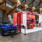 Toyota exhibition booth with red panels and a blue car on display inside a large, well-lit hall.