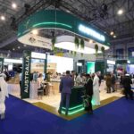 Australian trade expo booth with a large green circular overhead sign reading Australia, surrounded by visitors in a spacious convention hall