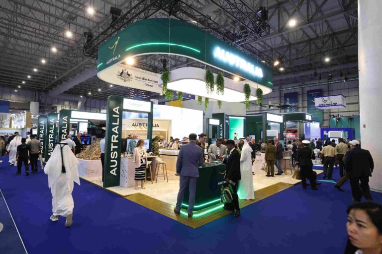 Australian trade expo booth with a large green circular overhead sign reading Australia, surrounded by visitors in a spacious convention hall